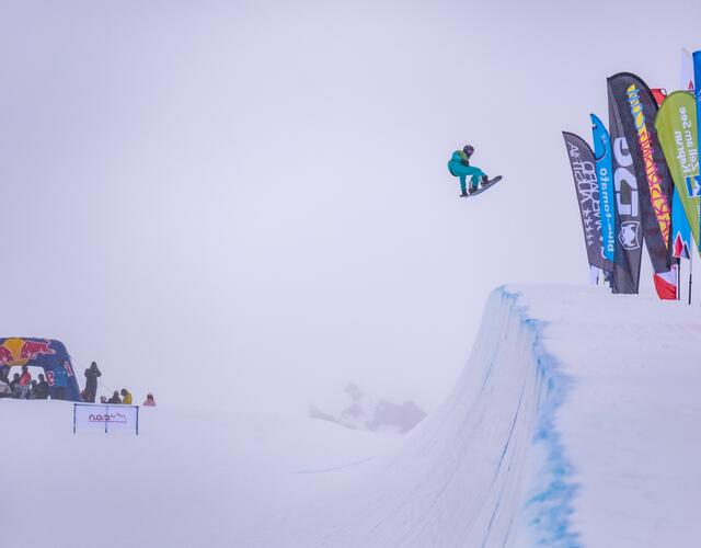 Snowboarder springt über eine Rampe vor verschneiter Kulisse