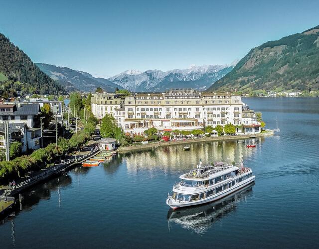 Ship at sea in front of hotel complex with mountains in the background | © Schmittenhöhebahn AG