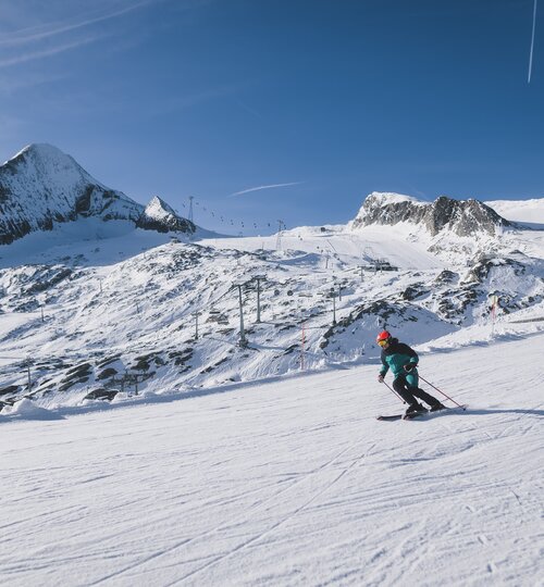 Skifahrer auf verschneiter Piste vor Bergkulisse