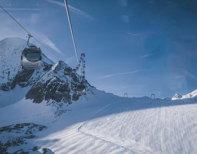 Seilbahngondeln über verschneitem Skigebiet unter blauem Himmel