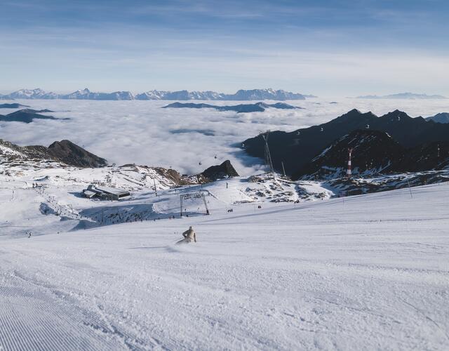 Skifahrer auf verschneiter Piste über Wolkenmeer