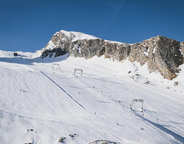 Breite verschneite Skipiste mit Skifahrern vor Bergkulisse