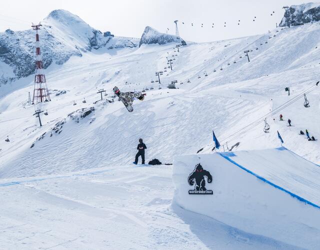 Snowboarder im Sprung über Schneerampe im Skigebiet