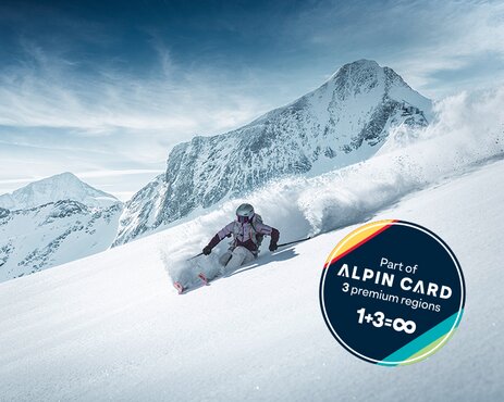 Skier skiing down a deep snow slope, with a snow-covered mountain and Alpin Card logo in the background