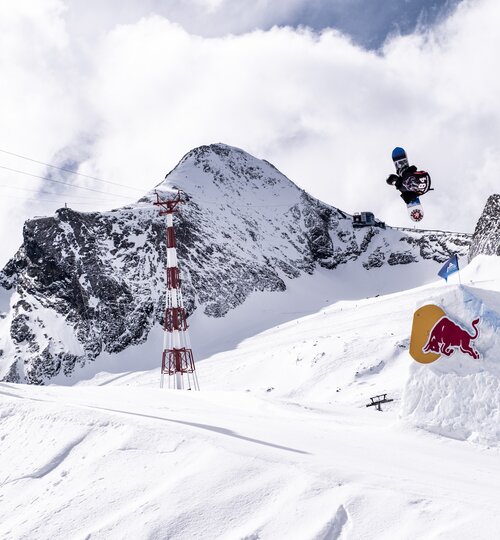 World Rookie Tour Finals am Kitzsteinhorn, ein Boarder springt auf einer Freestyle-Schanze mit Red Bull Logo und zeigt einen Trick, im Hintergrund das Kitzsteinhorn und Beachflags mit verschiedenen Logos | © Andreas Amplatz