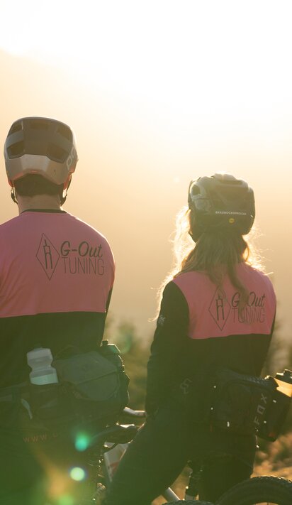 Zwei Mountainbiker mit pinkfarbenen Jacken vor Bergpanorama im goldenen Abendlicht | © Kitzsteinhorn 