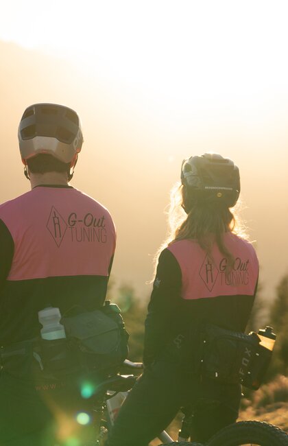 Zwei Mountainbiker mit pinkfarbenen Jacken vor Bergpanorama im goldenen Abendlicht | © Kitzsteinhorn 