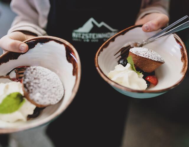 Zwei Hände halten Schüsseln mit Dessert: Kuchen, Sahne, Beeren und Puderzucker