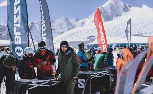 Skifahrer an Skistand vor verschneiter Bergkulisse