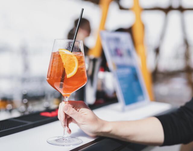 Hand hält Glas Aperitif mit Orangenscheibe