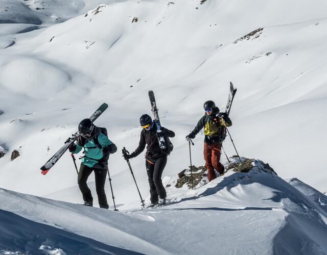 Risk'n'fun Freeride Campat the Kitzsteinhorn  | © Heli Fotoguide Three skiers carry skis on their backs and climb up a rock | © Heli Fotoguide