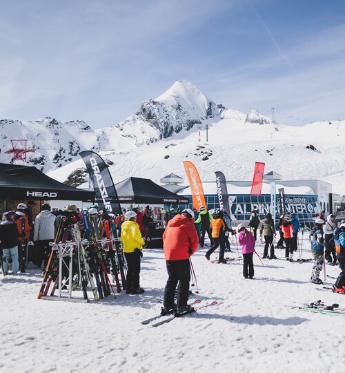 Many people on a ski slope testing equipment at stands of different ski companies, with the Kitzsteinhorn in the background. | © Kitzsteinhorn/Stefanie Oberhauser