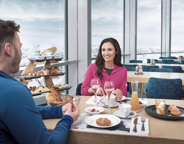Happy couple having breakfast in front of an Alpine panorama