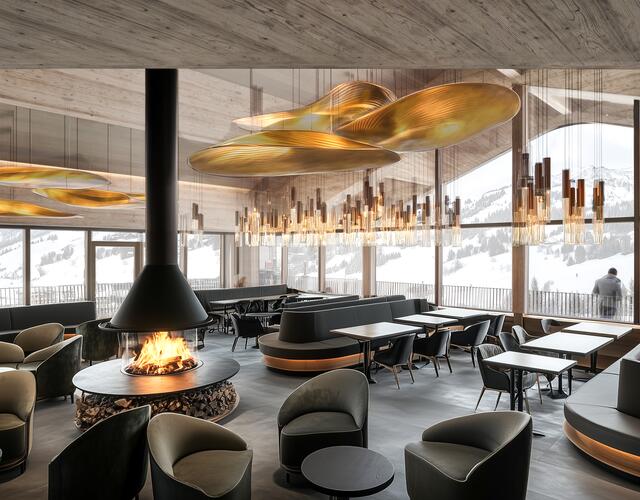 Innenansicht eines Restaurants mit Kamin, Tischen, Stühlen und goldfarbenen Lampen unter einer Holzdecke