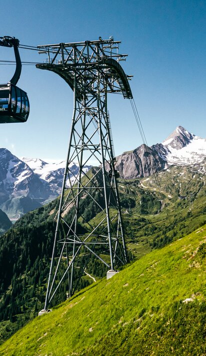 Seilbahn fährt über grüne Hügel mit schneebedeckten Bergen im Hintergrund | © Kitzsteinhorn 