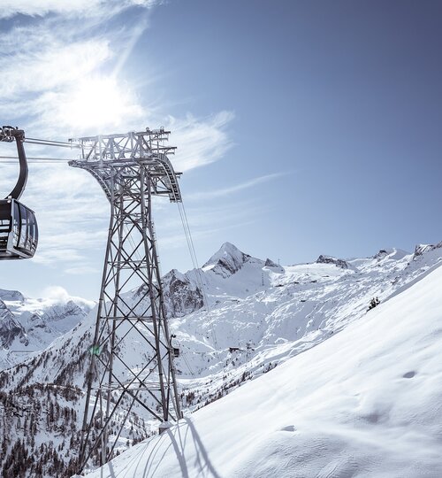 Cable car passes a steel mast in front of snow-covered mountains