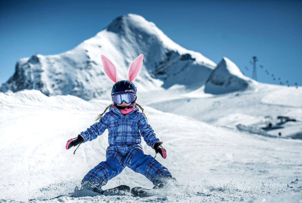 Skifahrendes Kind mit Hasenohren vor Bergkulisse
