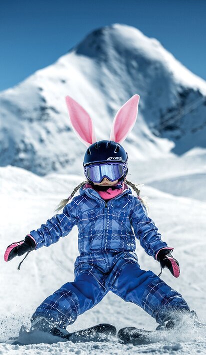 Skifahrendes Kind mit Hasenohren vor Bergkulisse