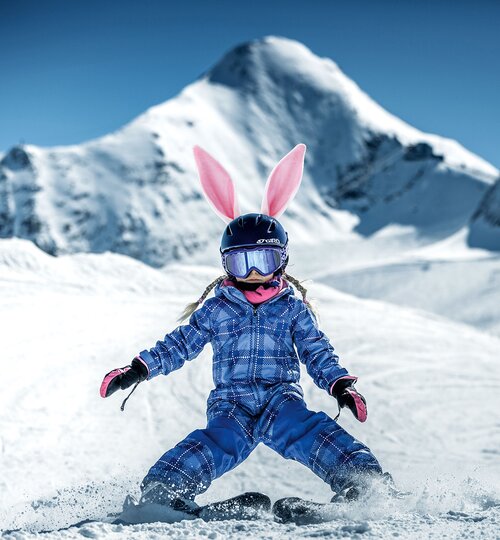 Skifahrendes Kind mit Hasenohren vor Bergkulisse