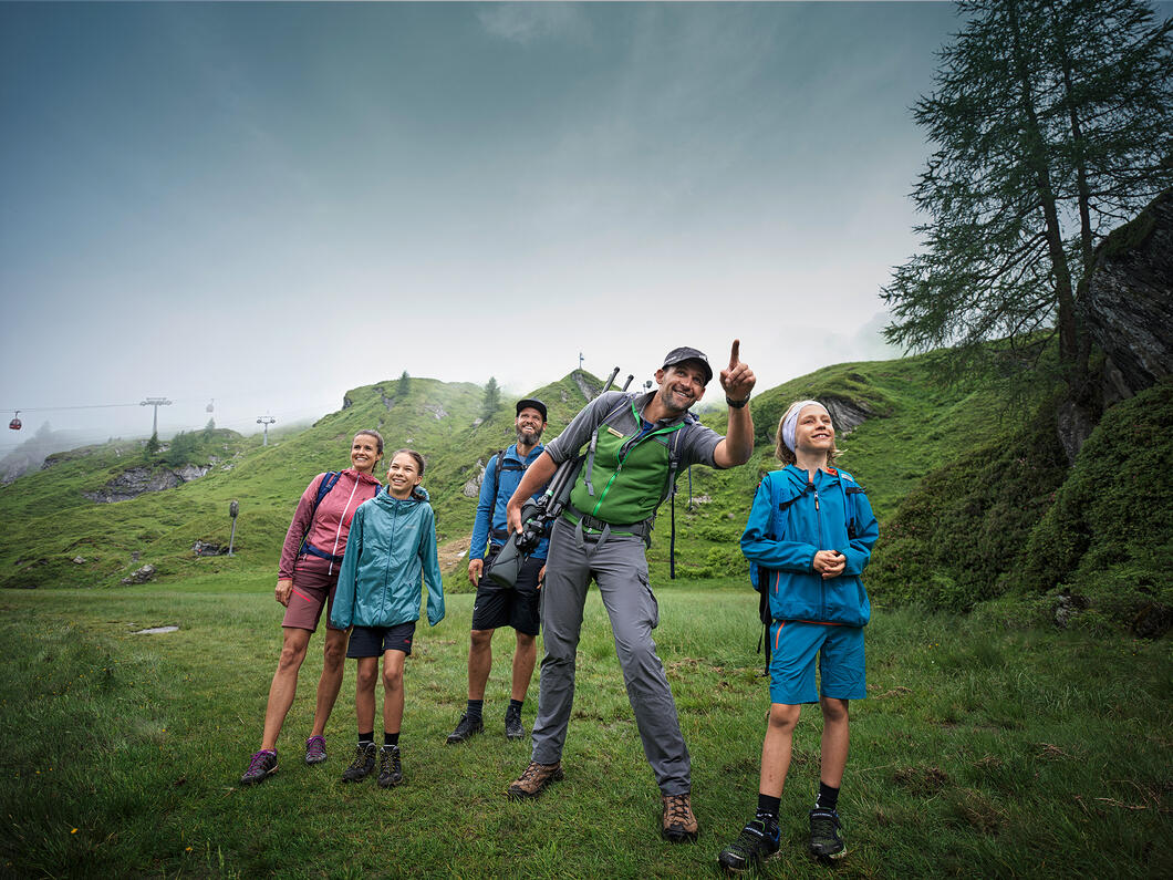 Wandergruppe mit Mann, Frau und Kindern auf grüner Wiese vor Berglandschaft