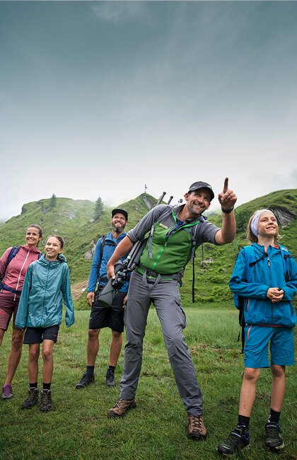 Hiking group with man, woman and children on green meadow in front of mountain landscape