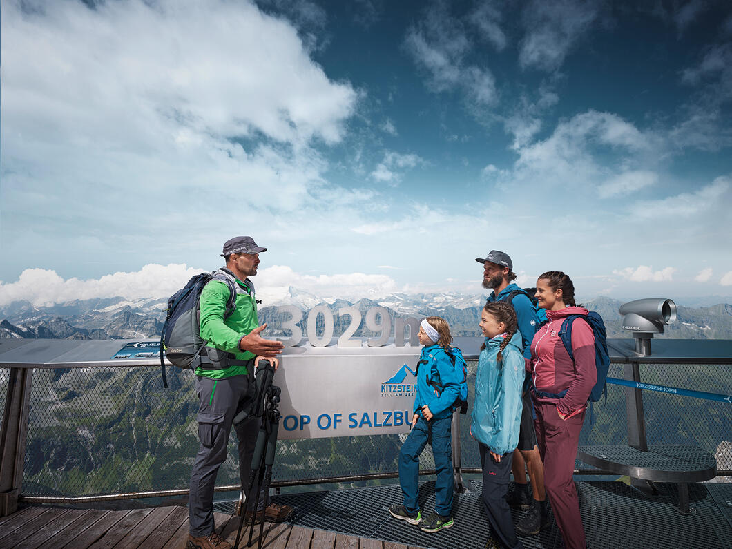 Wandergruppe vor Bergpanorama mit Gipfelkreuz und Wolkenhimmel