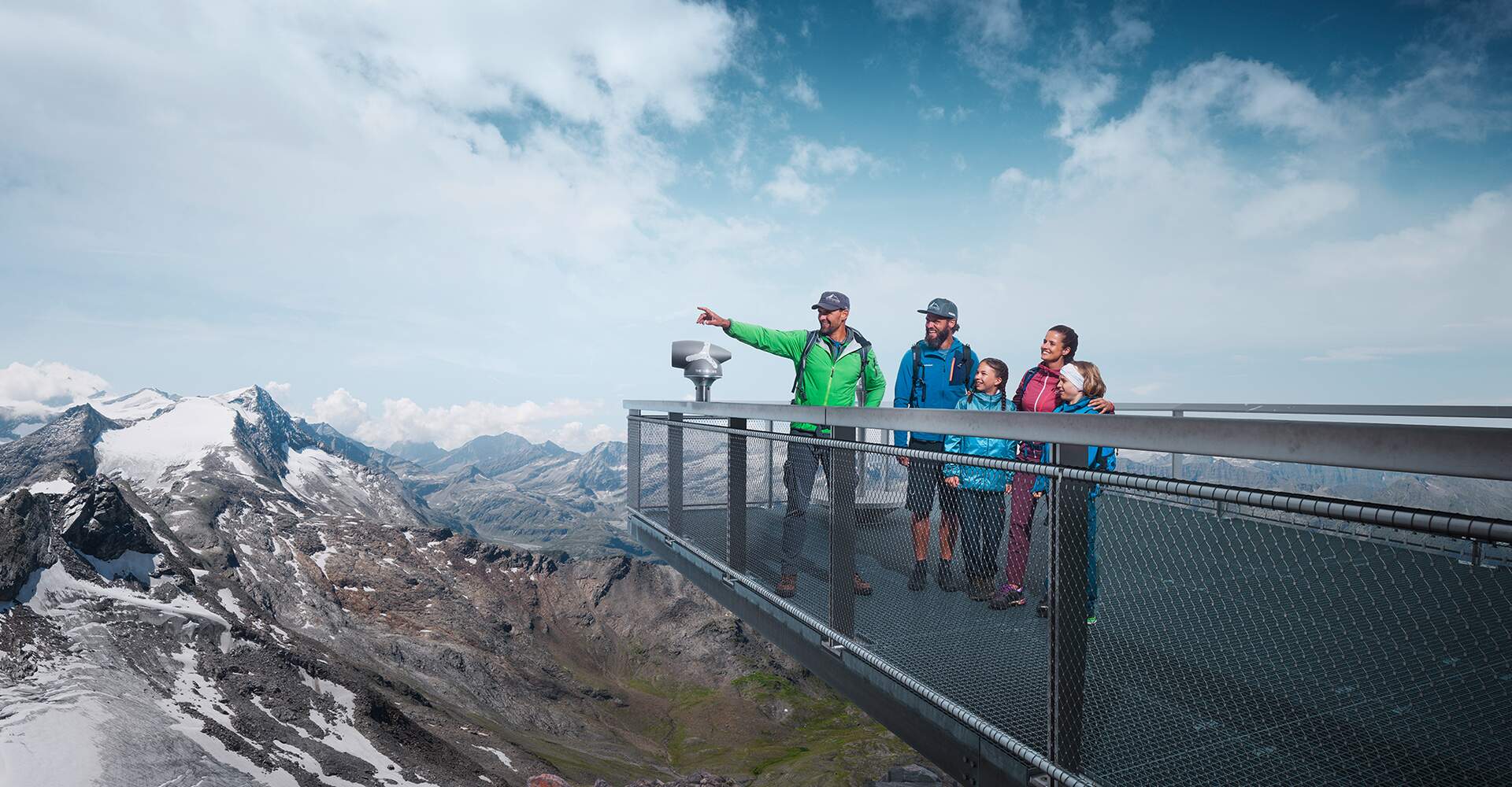 Family on viewing platform in the mountains, man pointing into the distance, snow-capped peaks