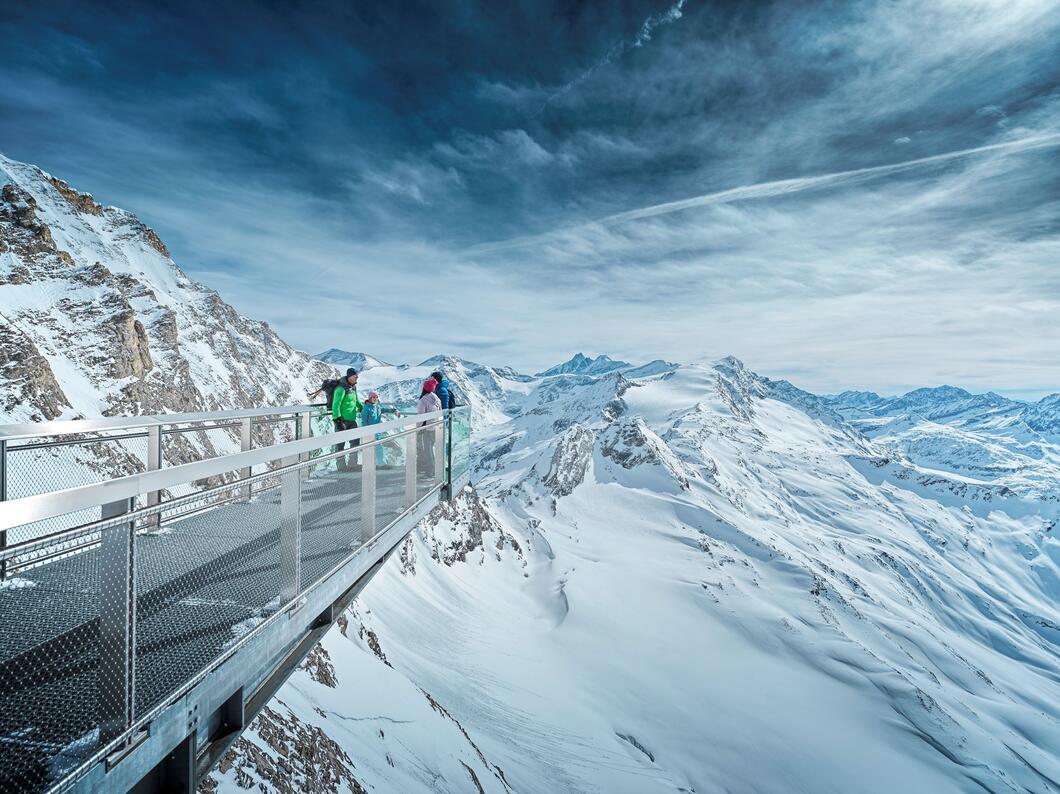 People on observation platform in snowy mountain landscape under cloudy sky