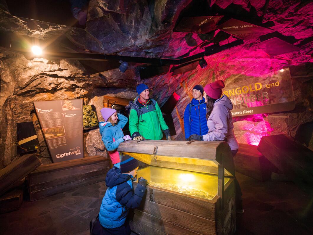 Familie öffnet Schatzkiste in dunkler Höhle mit Felsen und farbiger Beleuchtung