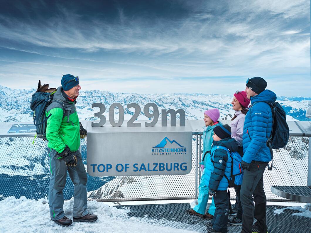 Familie steht am Gipfel des Kitzsteinhorns im Schnee vor einem Schild