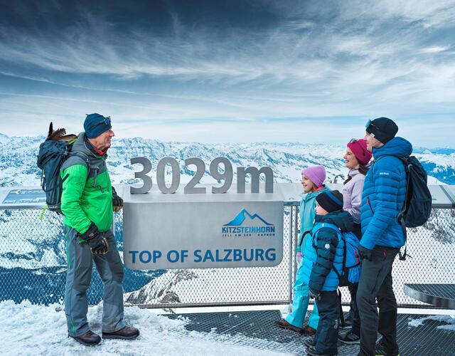Family standing in the snow in front of a sign at the summit of the Kitzsteinhorn