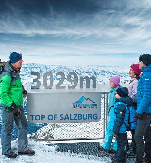 Family standing in the snow in front of a sign at the summit of the Kitzsteinhorn