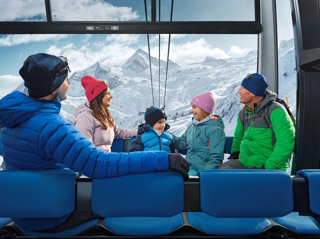 Familie in Gondel vor verschneiter Berglandschaft