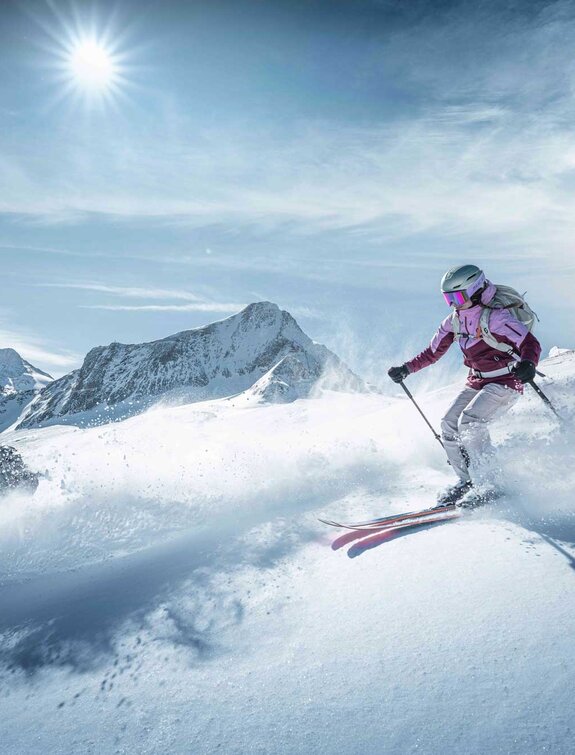 Freeriderin fährt Ski im Tiefschnee am Kitzsteinhorn bei strahlendem Sonnenschein