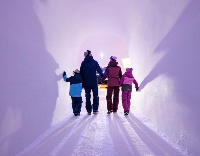 Familie in Winterkleidung im lilafarbenen Eistunnel
