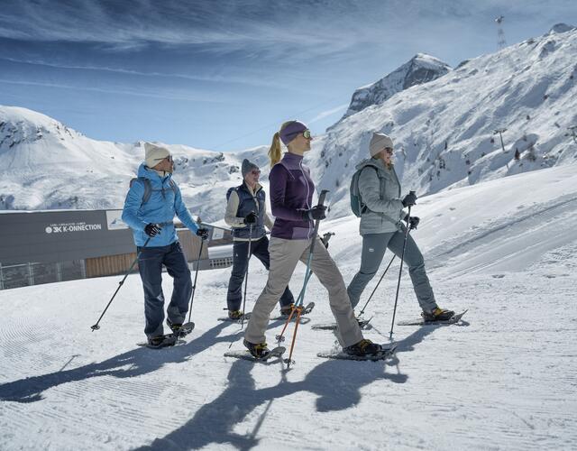 Four winter hikers walk a winter trail at the Kitzsteinhorn, beautiful scenery, with the station building of the 3K-Konnection in the background | © Kitzsteinhorn 