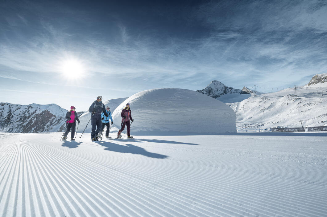 Vier Winterwanderer gehen einen Winterwanderweg am Kitzsteinhorn, schöne Landschaft, Ice Camp Iglus und das Kitzsteinhorn im Hintergrund | © Kitzsteinhorn 