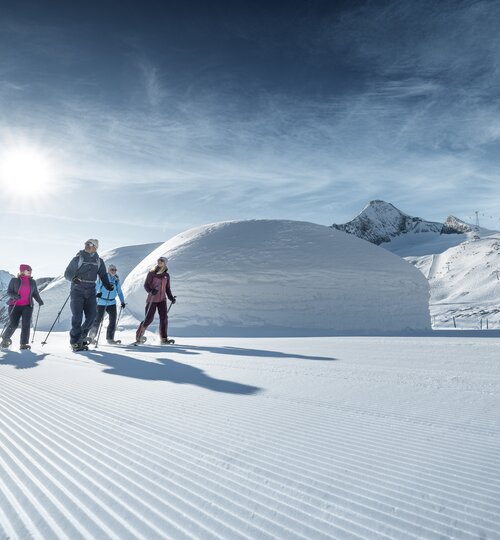 Four winter hikers walk a winter trail at the Kitzsteinhorn, beautiful scenery, Ice Camp igloos and the Kitzsteinhorn in the background | © Kitzsteinhorn 