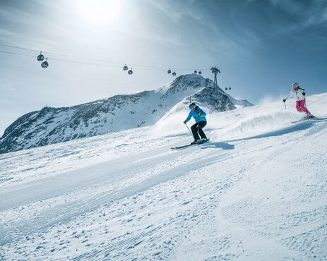Skiers on snow-covered slopes at Kitzsteinhorn Glacier with cable cars in the background