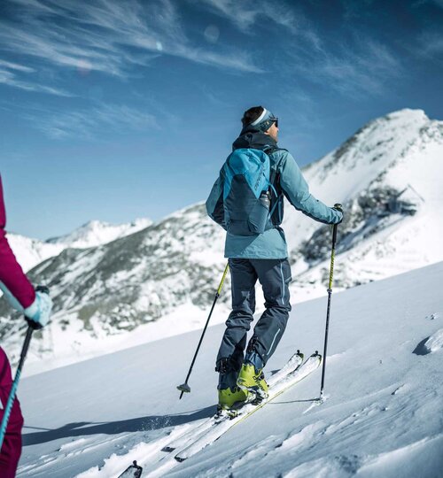 Ski tourer with backpack and skis in the snow in front of mountain panorama