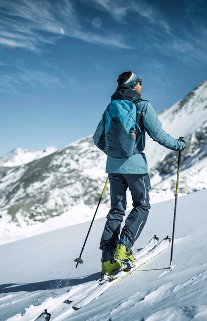 Skitourengeher mit Rucksack und Skiern im Schnee vor Bergpanorama