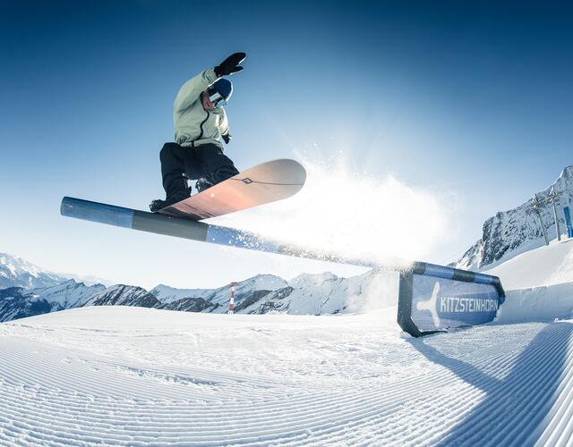 Snowboarder springt über Rail im Snowpark Kitzsteinhorn vor verschneiter Bergkulisse | © Kitzsteinhorn