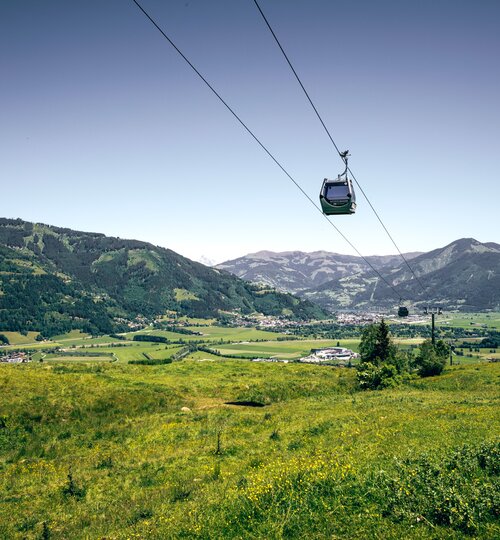 Cable car over green meadows and hills in front of a mountain panorama on a sunny day